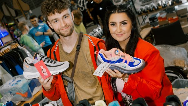 Two people holding sneakers at a sneaker convention.