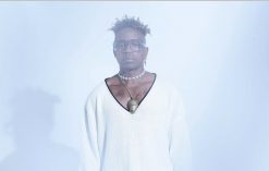 Blick Bassy posing in front of a white background wearing a white shirt.