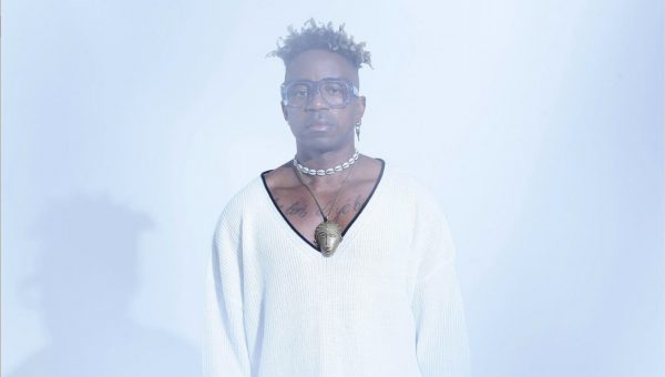 Blick Bassy posing in front of a white background wearing a white shirt.